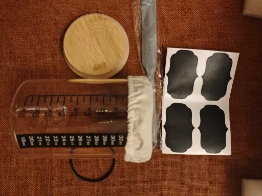 Wooden lid, cloth cover, chalk label sheet and elastic bands laid out beside the graduated jar