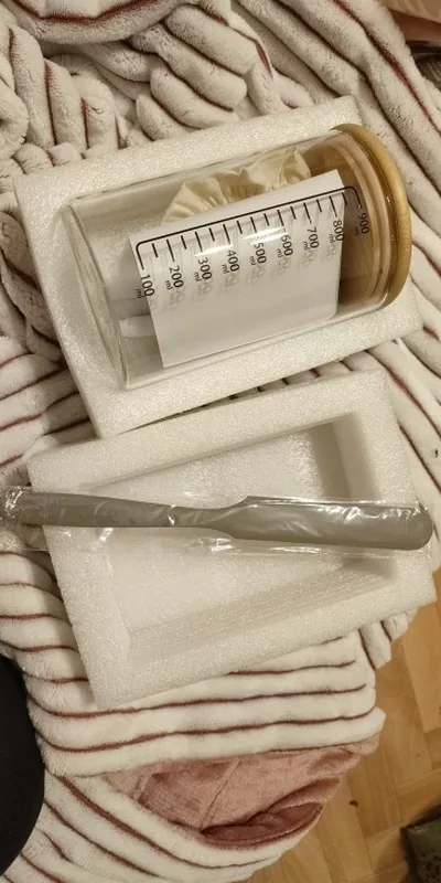 The jar lying in its protective foam with the wooden lid on, the milliliter scale readable down the side, and the spatula alongside